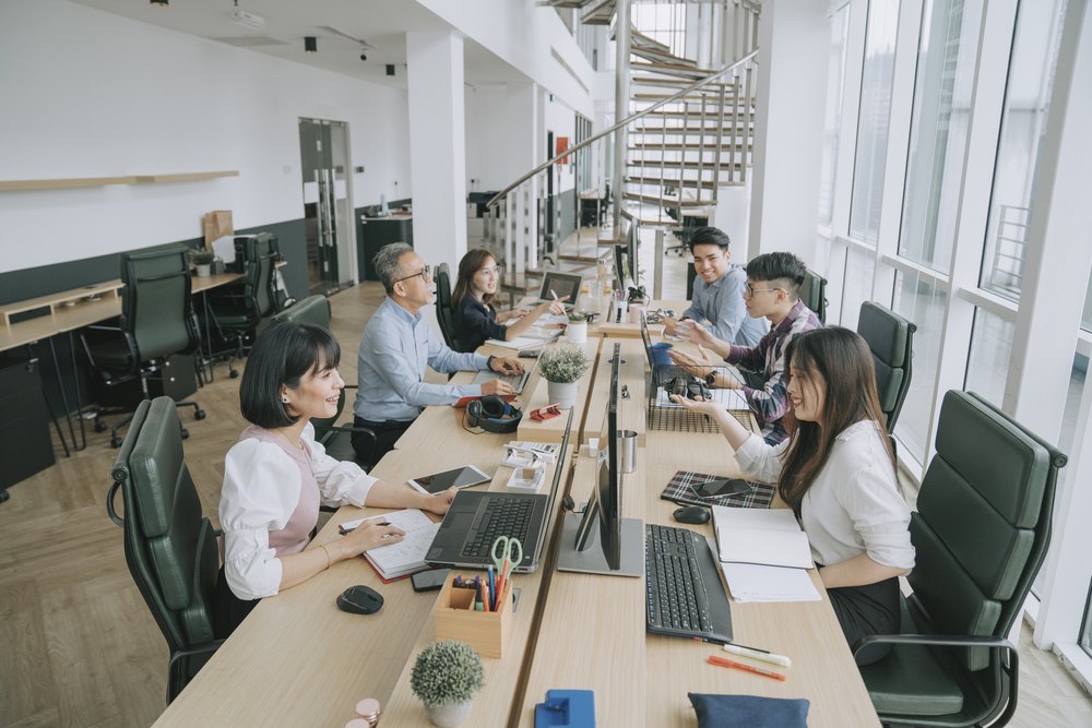 Multi-ethnic professionals working along a shared desk in an open-plan office, representing the range of roles Australian SMEs can offshore